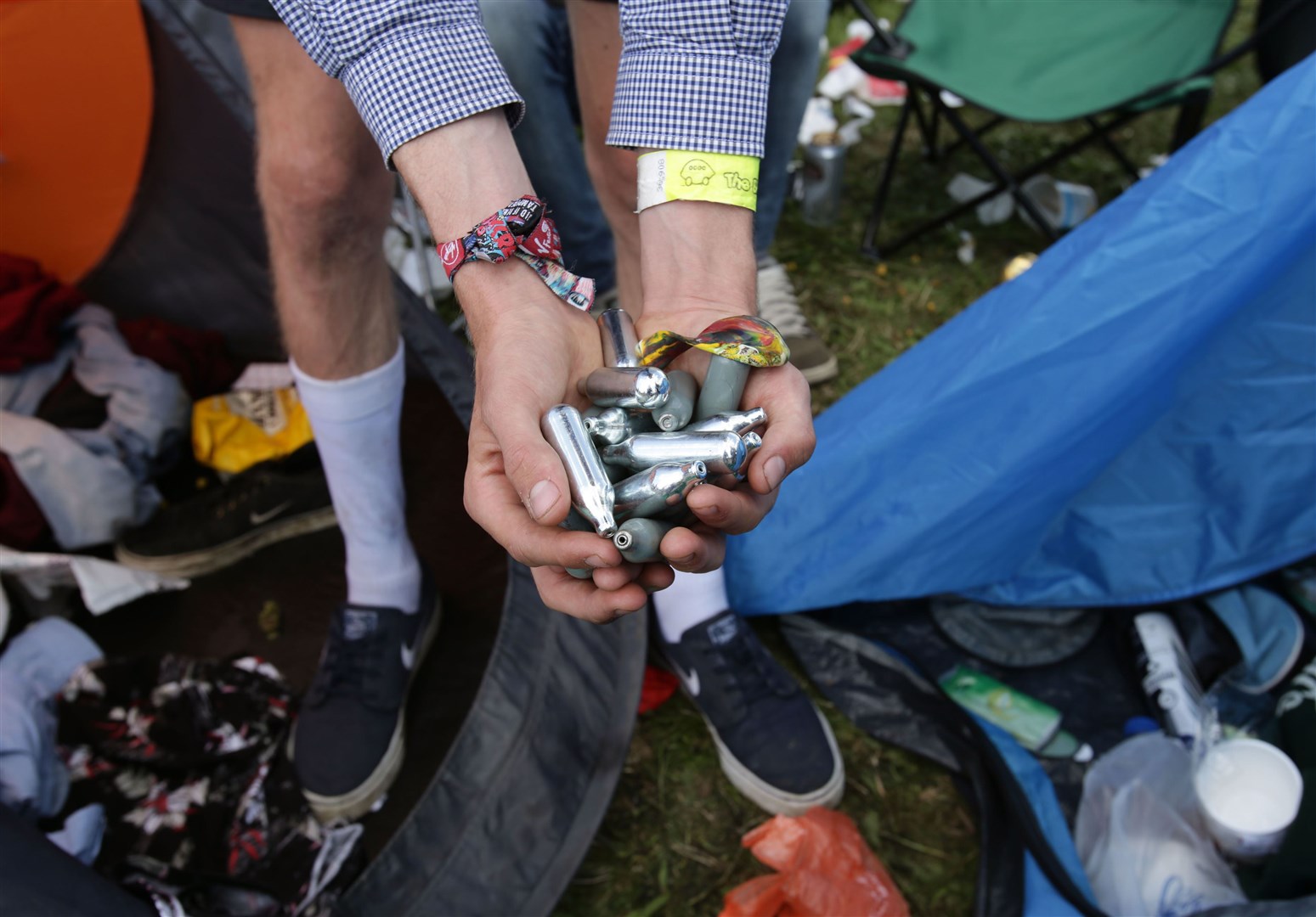 A festivalgoer holding a handful of spent laughing gas canisters in a campsite at Reading Festival in 2014 (PA)
