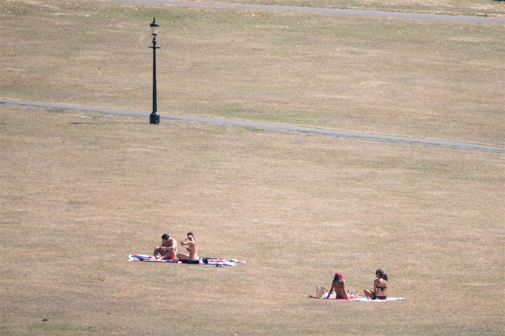 People sit on the dry grass of Primrose Hill, north London (Dominic Lipinski/PA)