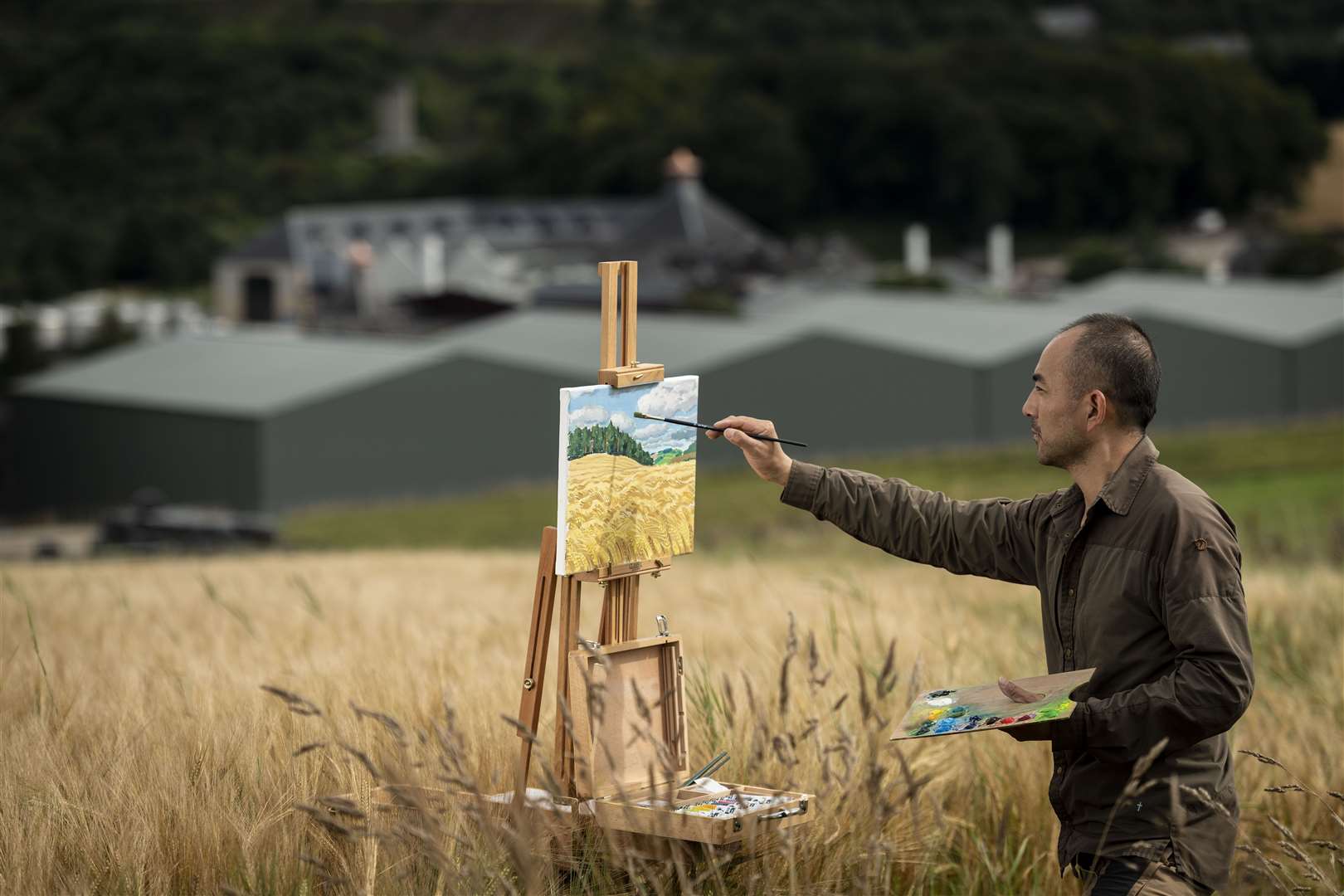 Chinese artist Guo Haiqiang painting in barley fields above Glenfiddich Distillery in Dufftown.