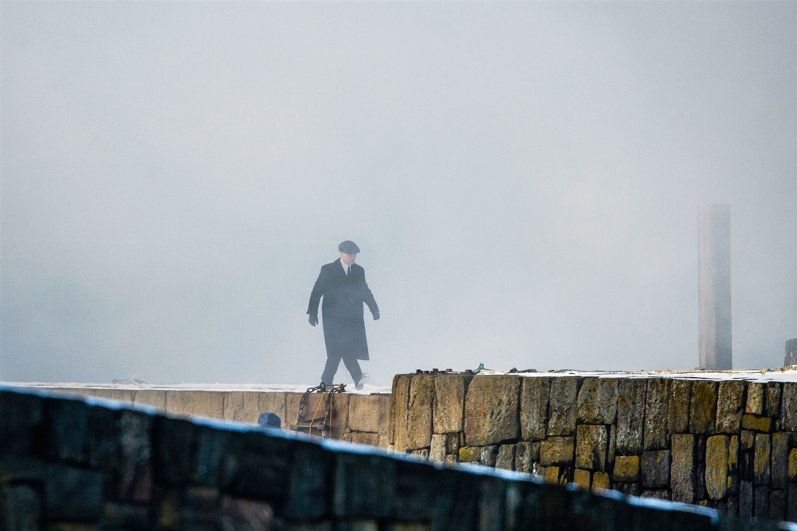 Peaky Blinders character Tommy Shelby, played by Cillian Murphy, walks along Portsoy's old harbour pier through artificial smoke during filming in February. Picture: Daniel Forsyth.
