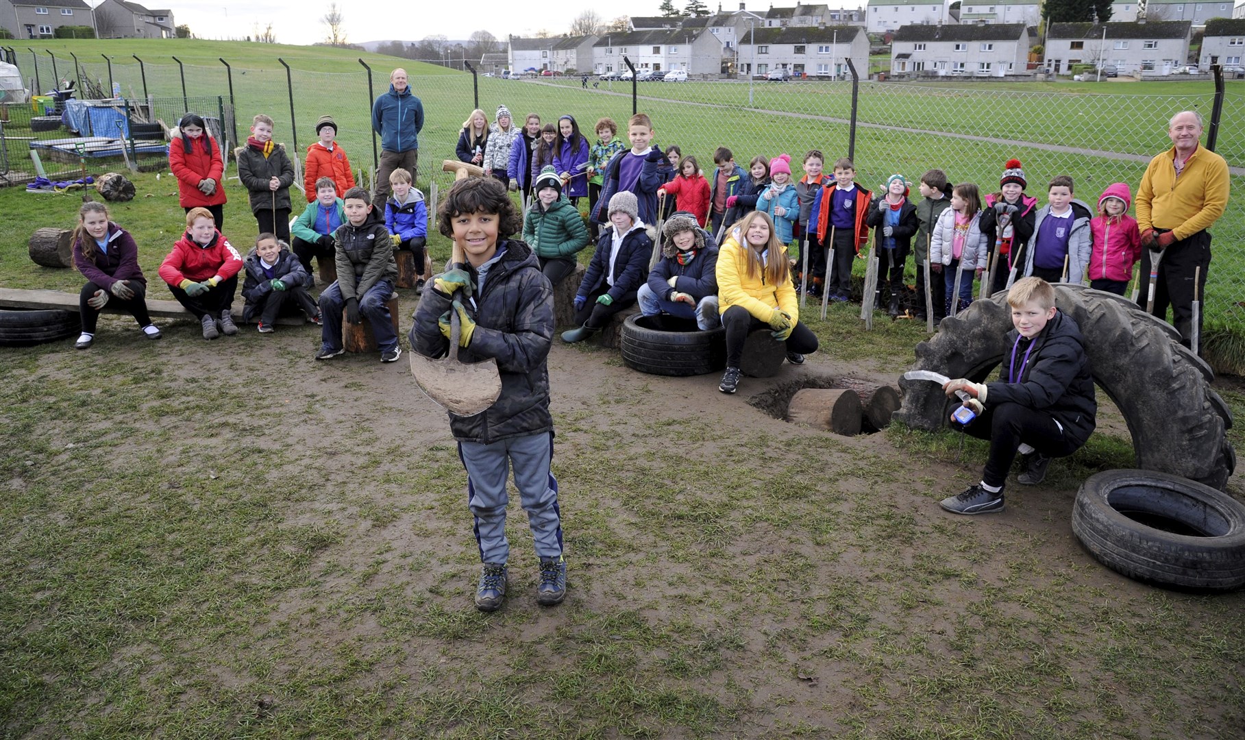 Primary 5/6 pupil Ty Ravello in the foreground, with pupils planting trees at Seafield Primary School.
