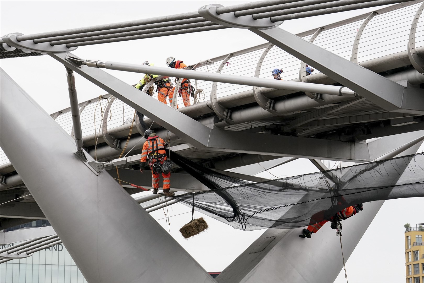 A straw bale is suspended from London’s Millennium Bridge as work is undertaken on the structure (Jordan Pettitt/PA)
