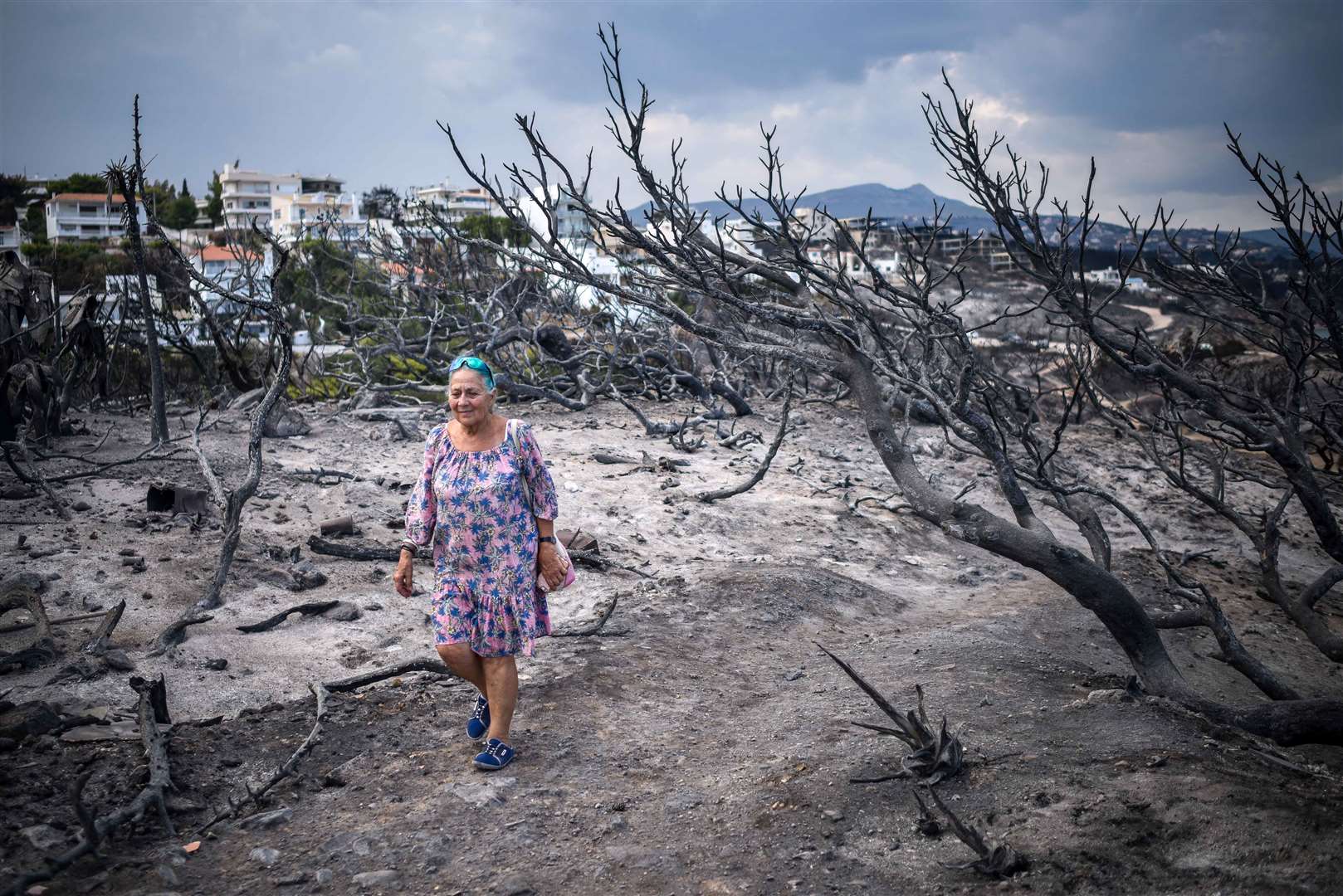 An elderly woman walks through an area of burnt bushes in Rafina, Greece on July 25 2018. Wildfires ravaged houses and properties in the seaside resort earlier this week, killing 79 people.