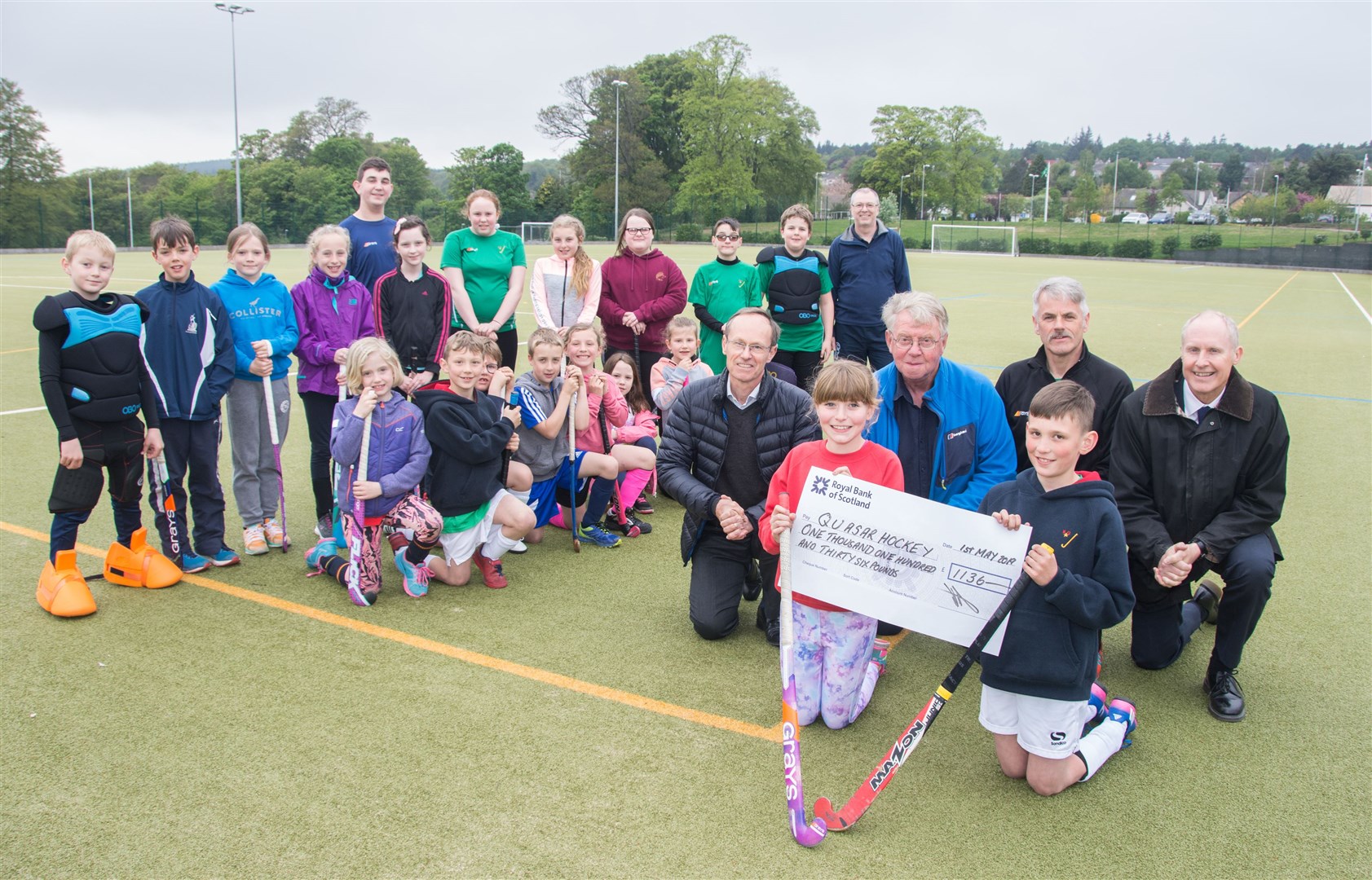 Quasar players (front) Zoe Beange and Fergus Smith, with coach Pete Bavidge (middle second right), receive a cheque from Moray Hockey Club members (middle from left) Jamie Watson, Bill Hope and Will Cowie during a training session at the Elgin Academy pitches. Picture: Becky Saunderson. Image No.043869.