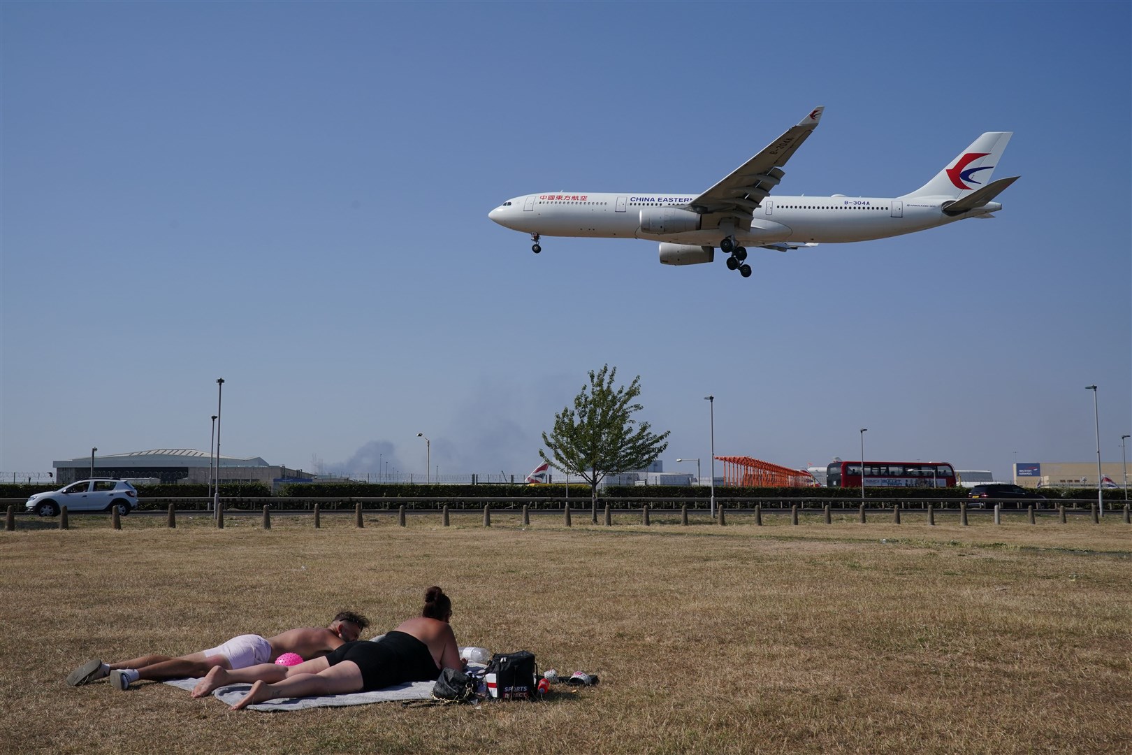 A couple sunbathe as a China Eastern flight comes into land at Heathrow Airport, London in July (Jonathan Brady/PA)
