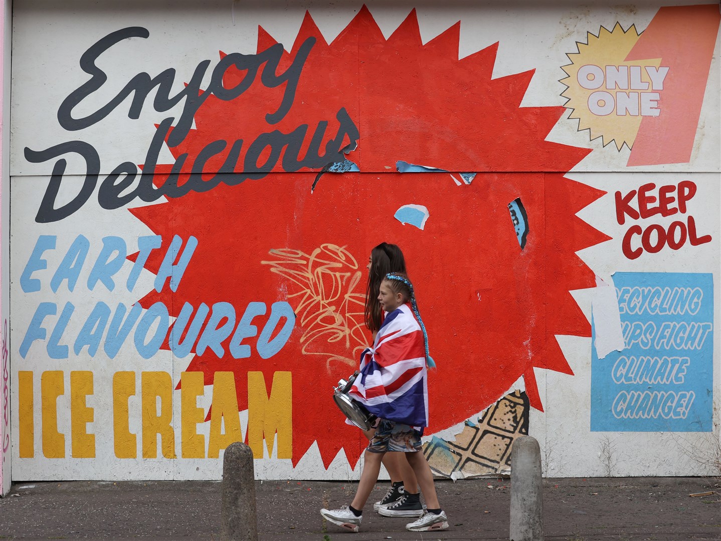 Two women walk past a sign after watching a Twelfth of July parade in Belfast (Liam McBurney/PA)