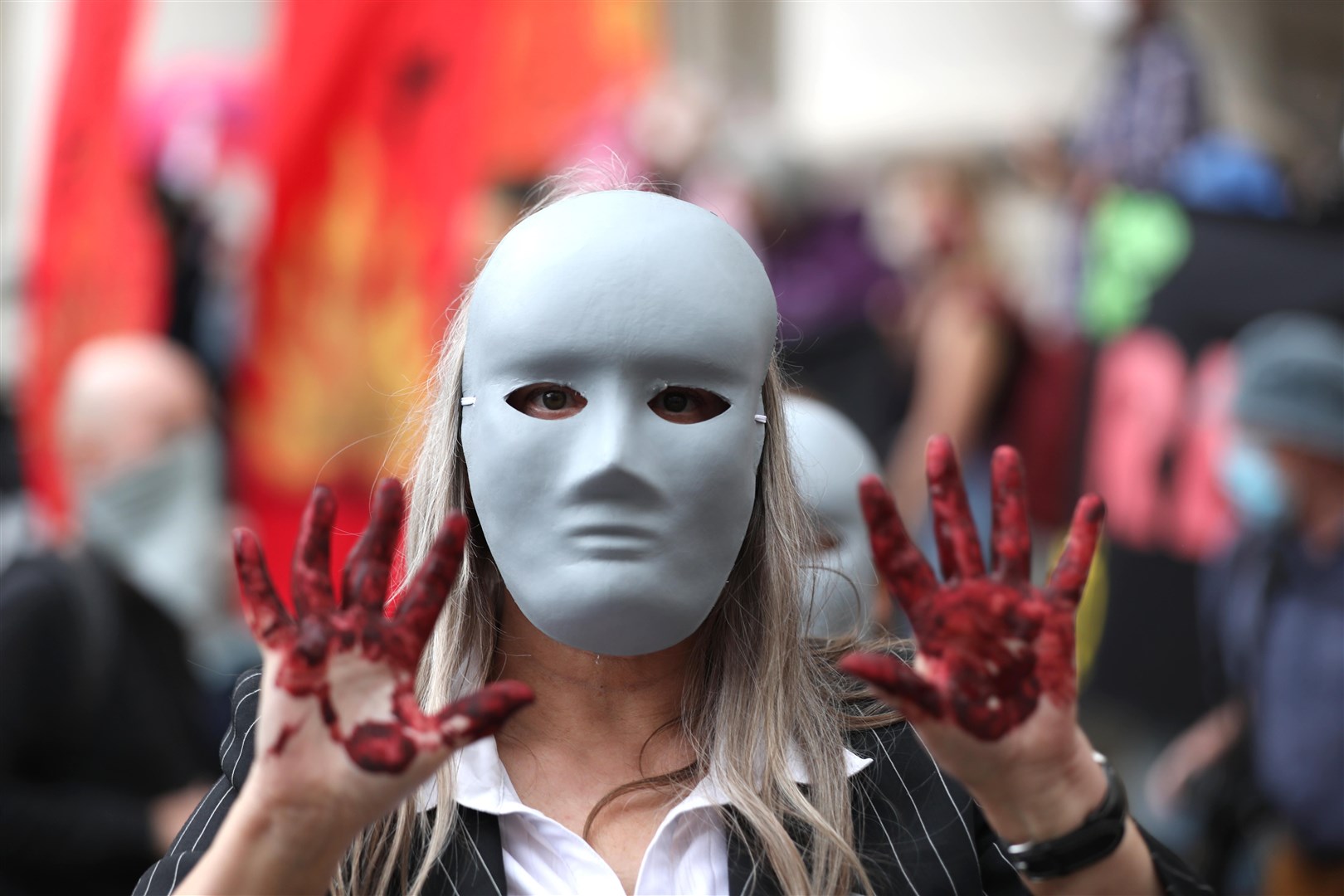 A masked protester, hands covered with fake blood, stands outside the Bank of England (Luciana Guerra/PA)