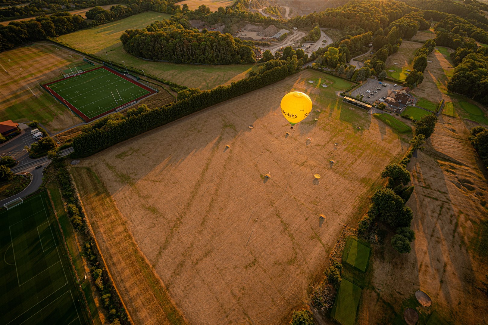 A hot air balloon flies over a browning and parched golf driving range early in the morning (PA)