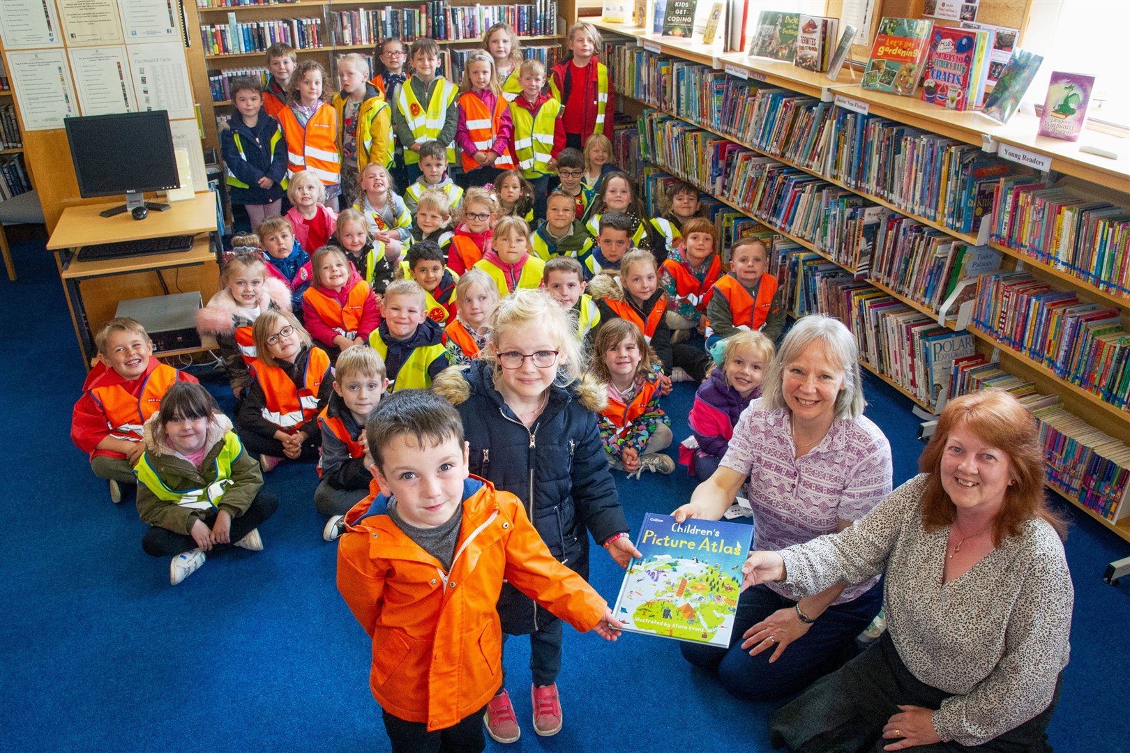 St Gerardine Primary School P1s present an atlas to Meriol Rattray and Jenn Hand at Lossiemouth Library