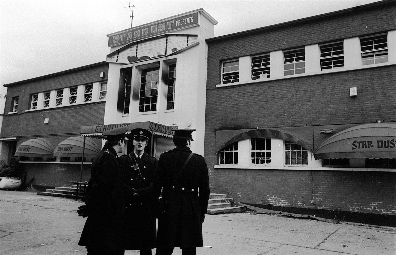 Police stand outside the main entrance of a fire-blackened Stardust Disco in Artane, Dublin, in 1981 (Tony Harris/PA)