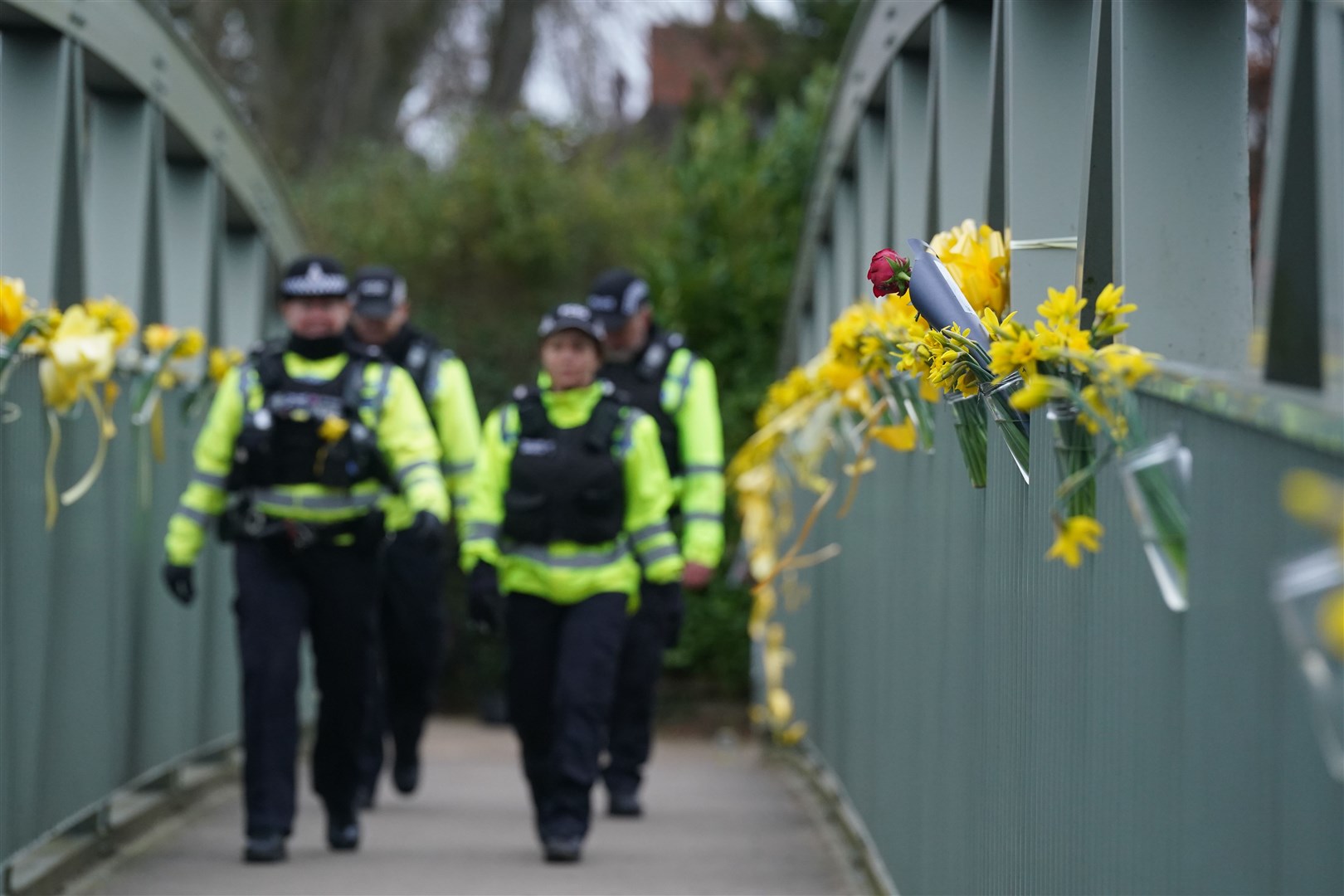 Police officers walk past flowers and yellow ribbons tied to a bridge for Nicola Bulley over the River Wyre in St Michael’s on Wyre, Lancashire, where police recovered a body on Sunday (Owen Humphreys/PA)