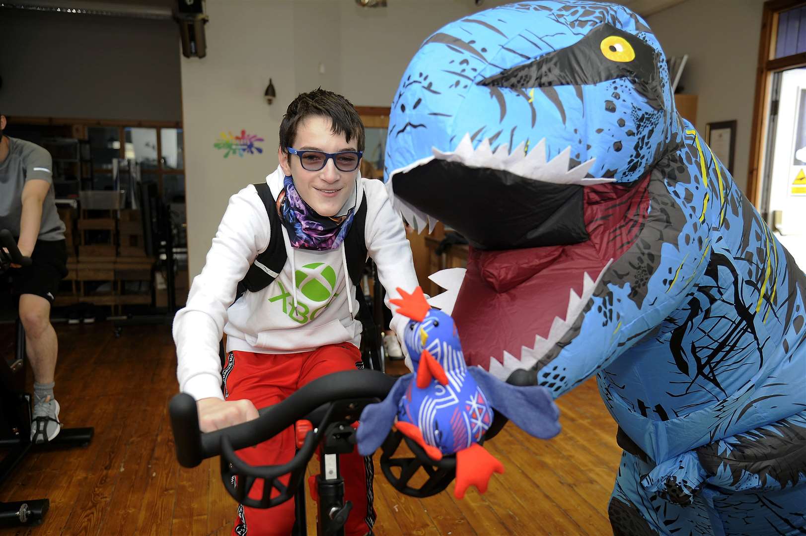 Archie Edwards puts in his cycle kilometres to help reach the collective 2000km target, supported by Riley Mclaggan, in a dinosaur costume. Picture: Becky Saunderson.