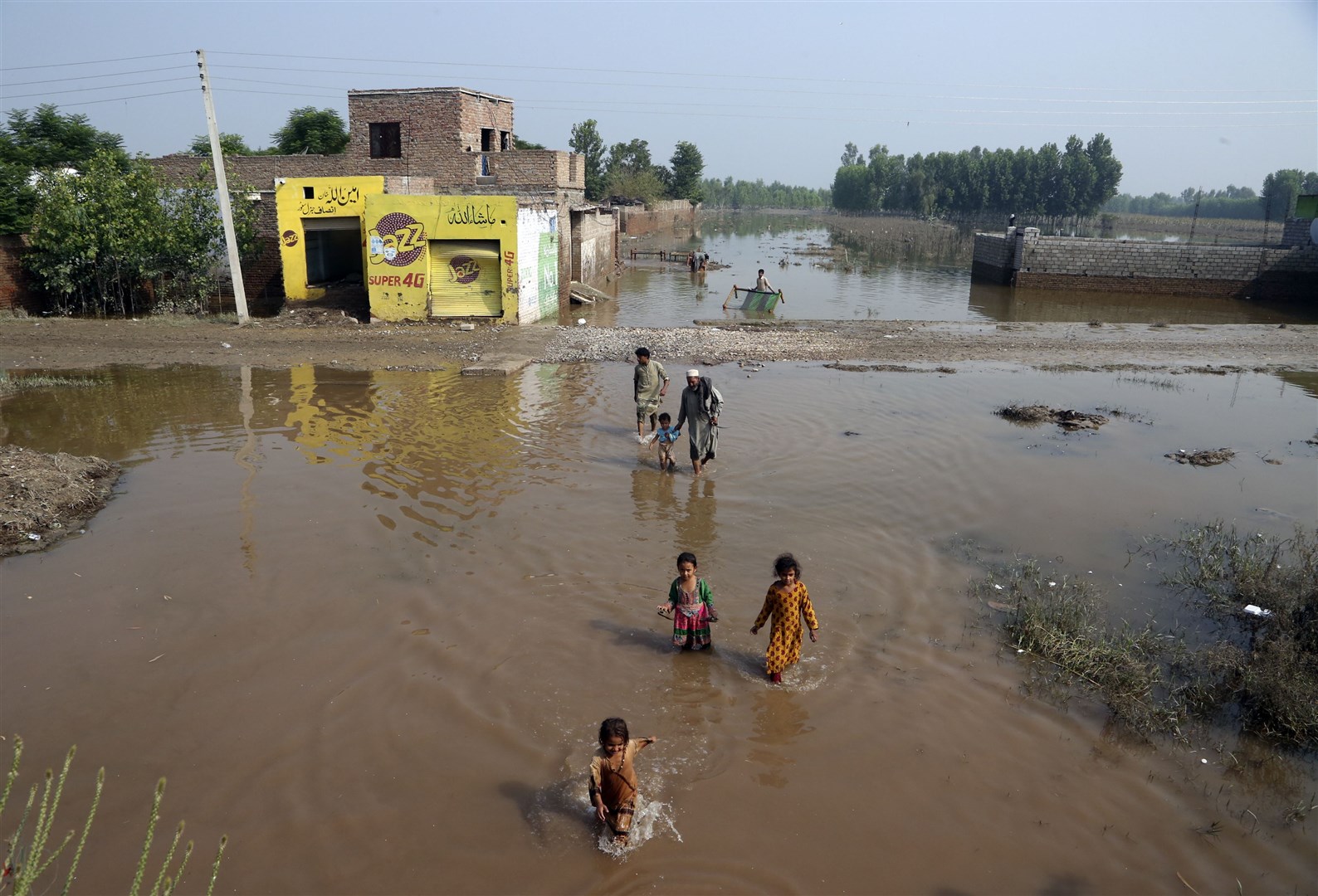 People wade through floodwaters in Charsadda, Pakistan (Mohammad Sajjad/AP)