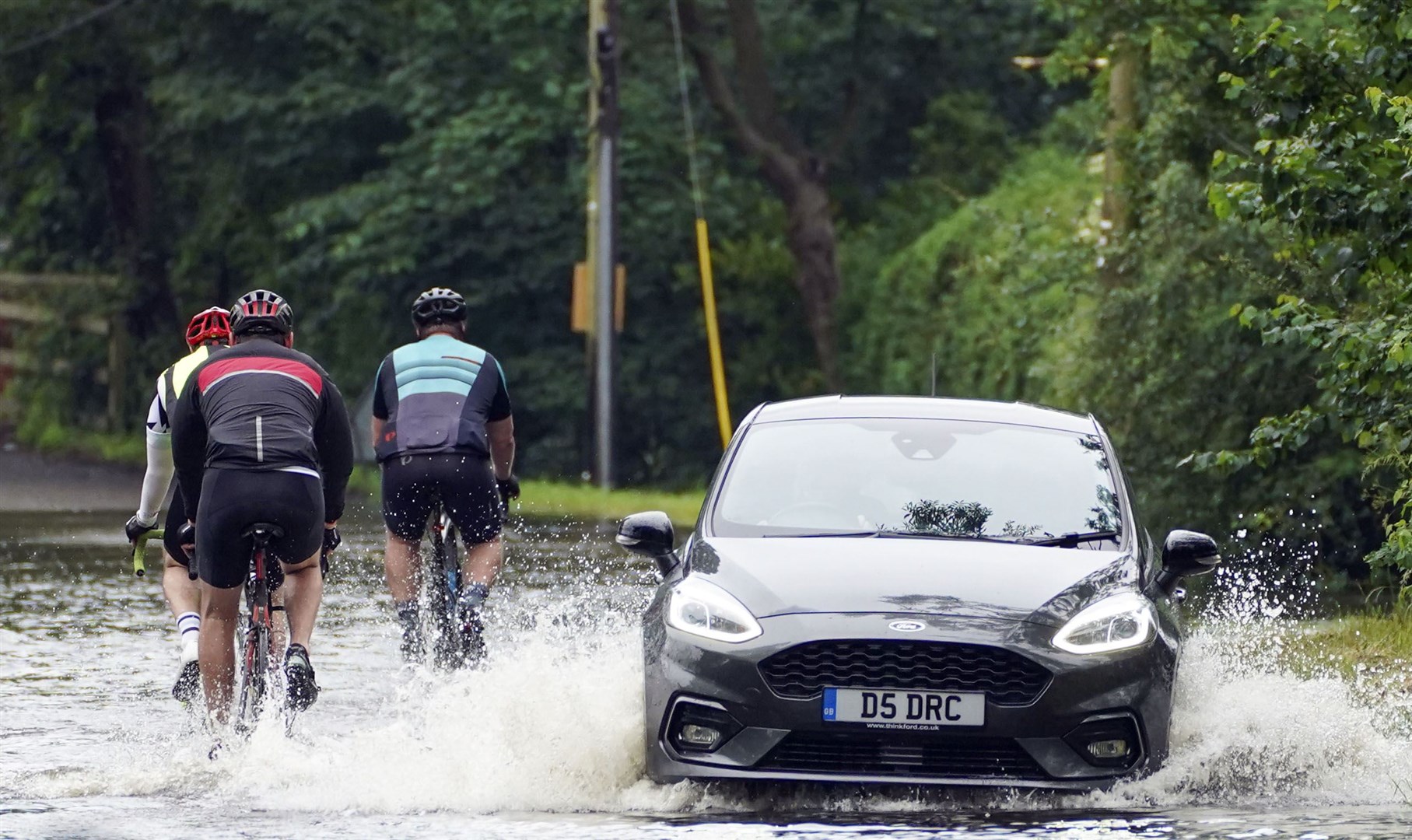 A car and cyclists pass on a flooded road near Swallowfield, Berkshire (Steve Parsons/PA)